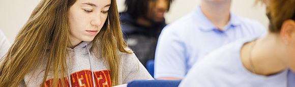 Image of four students in a classroom taking notes.